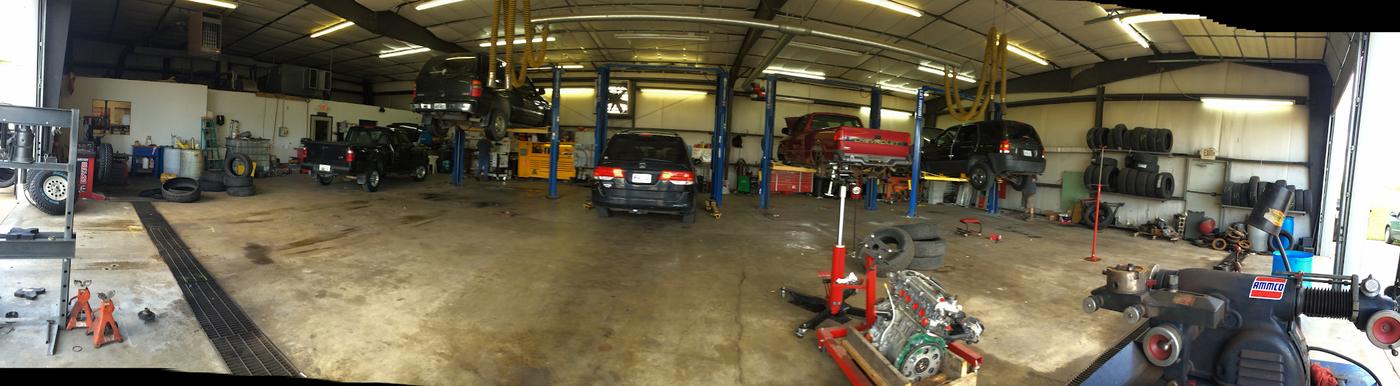 Panoramic view inside the workshop showing vehicle lifts, a wall of tires and an engine on a stand